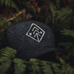 Close-up of a dark baseball cap with an embroidered design nestled among green ferns, creating a nature-themed concept.