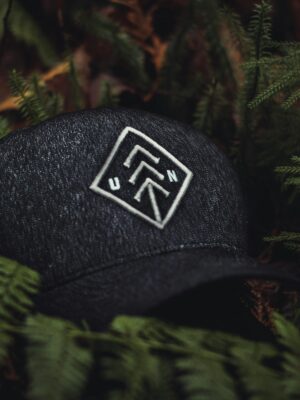 Close-up of a dark baseball cap with an embroidered design nestled among green ferns, creating a nature-themed concept.