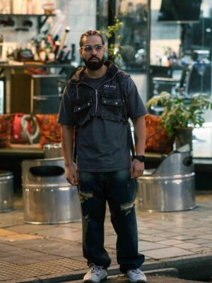 Portrait of a man in street style clothing outside a Tehran barbershop.